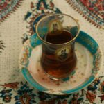 Persian-style black tea served in clear glasses with a teapot, dates and sugar cubes